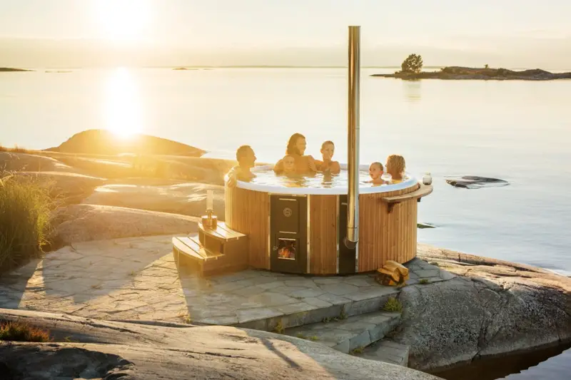 Des personnes profitant du bain nordique Skargards Rojal avec poêle intégré lors d'un coucher de soleil