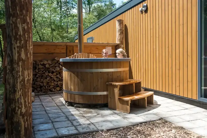 Bain nordique Ticra en Thermowood avec poêle interne installé à côté d'un chalet de vacances