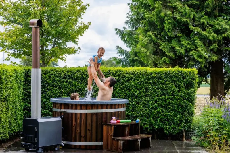Vader en dochter spelen in warme Ticra Thermowood hottub met externe houtgestookte kachel