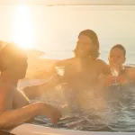 Des personnes profitant d'un verre dans le bain nordique Skargards Rojal avec poêle intégré au coucher du soleil