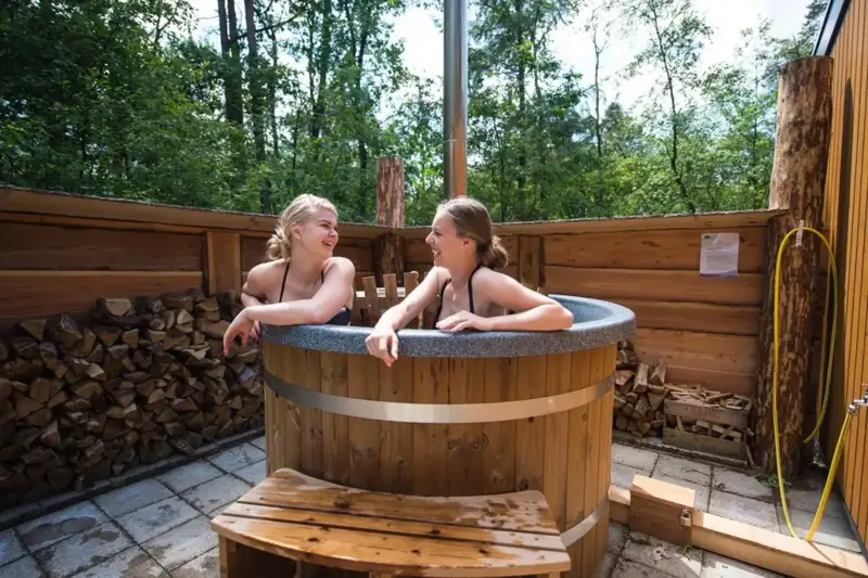 Personnes profitant du bain nordique Ticra en Thermowood avec poêle interne près d'un chalet
