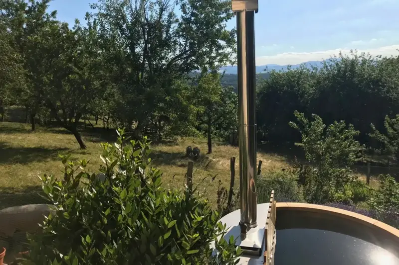 Bain nordique Ticra en Thermowood avec poêle interne dans un jardin ensoleillé avec vue panoramique sur la nature