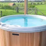 Vue avant du bain nordique Nordic Hottub Classic avec finition en cèdre rouge et marches en cèdre rouge dans un pré