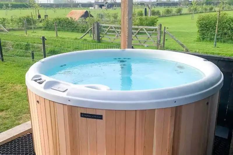 Vue avant du bain nordique Nordic Hottub Classic avec finition en cèdre rouge et marches en cèdre rouge dans un pré