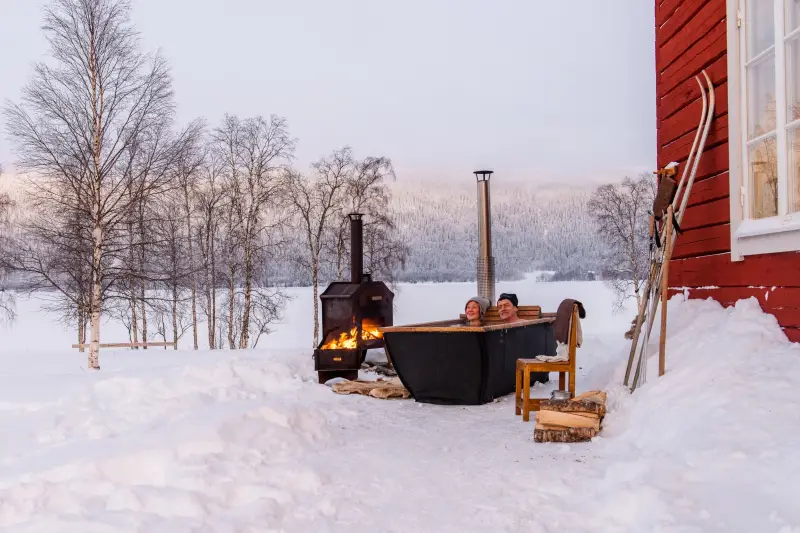 Couple profitant du bain nordique Hikki Bohemen chauffé au bois dans la neige