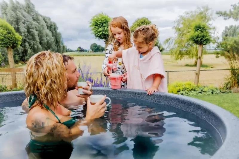 Vader en moeder genieten van koffie in warme hottub terwijl kinderen spelen in de tuin