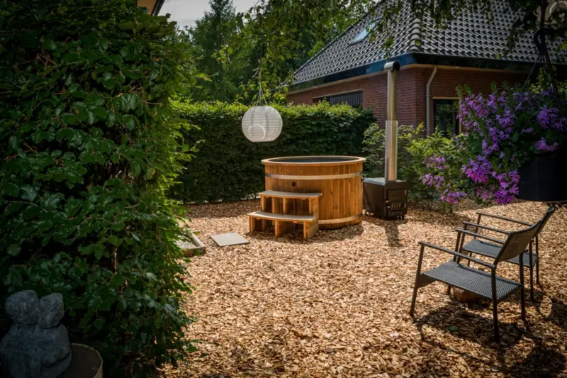Ticra Thermowood hottub met externe 45 kW houtgestookte kachel in zonnige bloeiende tuin