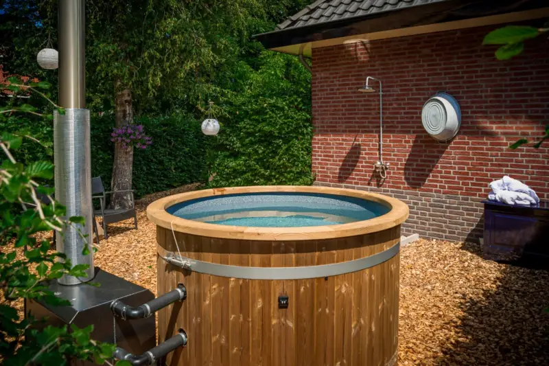 Mooie Ticra Thermowood hottub geplaatst in zonnige boerderijtuin met externe houtgestookte kachel