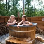 Personnes profitant du bain nordique Ticra en Thermowood avec poêle interne près d'un chalet