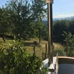 Bain nordique Ticra en Thermowood avec poêle interne dans un jardin ensoleillé avec vue panoramique sur la nature