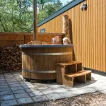 Bain nordique Ticra en Thermowood avec poêle interne installé à côté d'un chalet de vacances