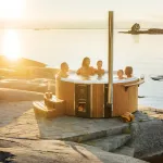 Des personnes profitant du bain nordique Skargards Rojal avec poêle intégré lors d'un coucher de soleil