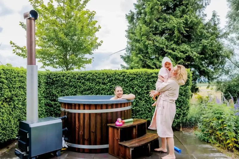 Ticra Thermowood hottub met externe 45 kW houtgestookte kachel en blij gezin in de tuin