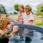 Vader en moeder genieten van koffie in warme hottub terwijl kinderen spelen in de tuin
