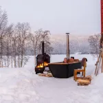 Couple profitant du bain nordique Hikki Bohemen chauffé au bois dans la neige